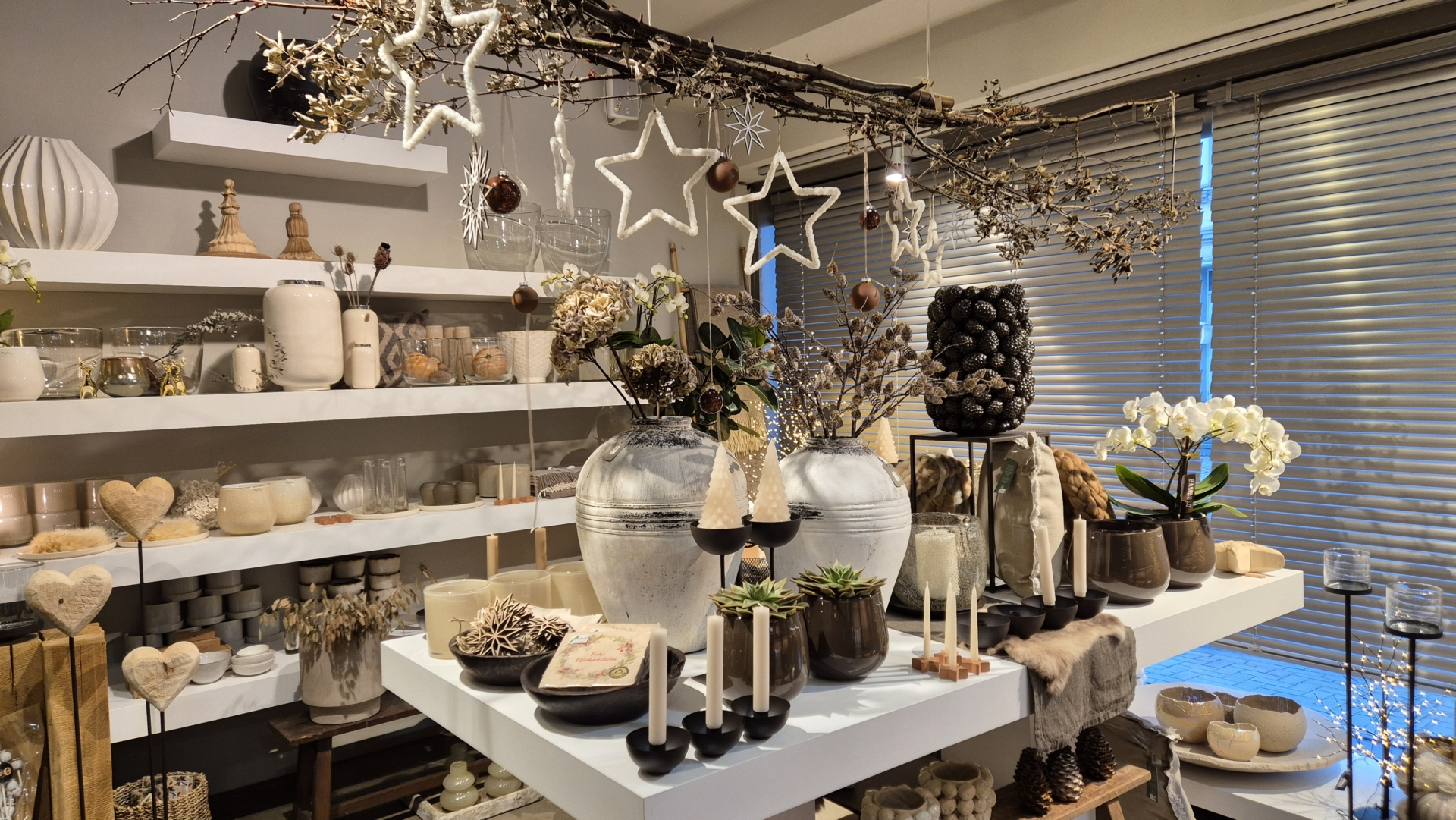 Dekorative Arrangements mit Pflanzen, Kerzen und Glasgefäßen auf einem weißen Tisch in einem Geschäft für Innendekoration.
