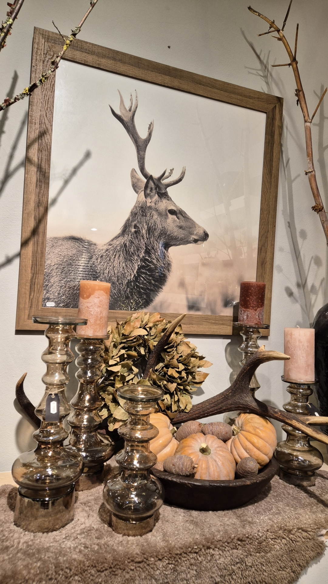 Ein Hirschbild in einem Holzrahmen, umgeben von Kerzenhaltern, Kürbissen und Geweihen auf einem Tisch.