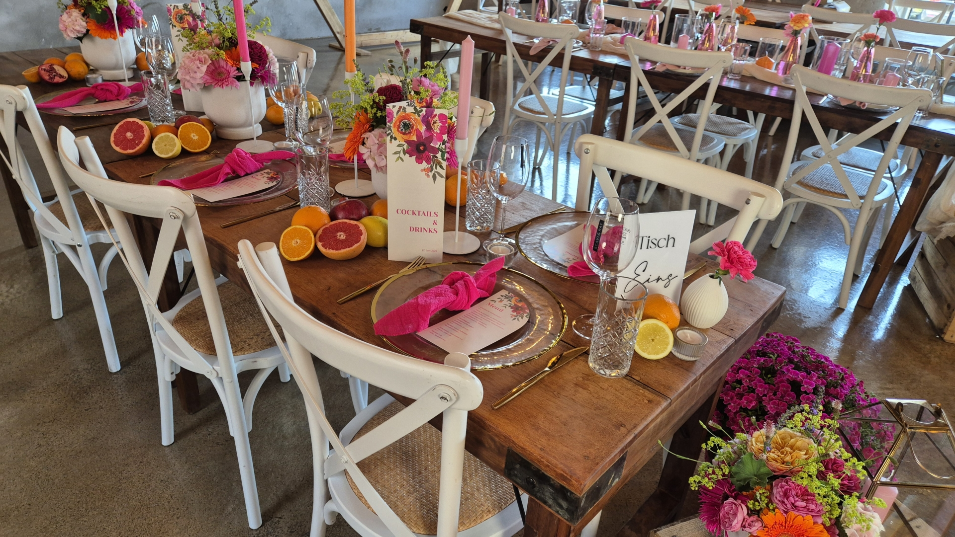 Tischdekoration mit bunten Blumen, Geschirr und frischen Früchten auf einem Holztisch in einem festlichen Arrangement.